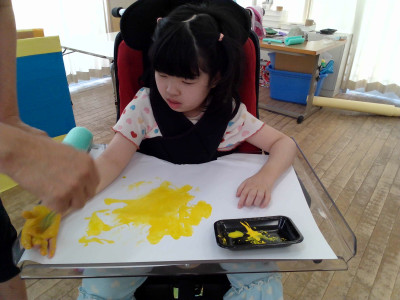 手のひらを使って絵の具を画用紙に塗り、色の混ざり具合を楽しんでいます。