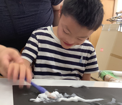 泡絵の具を筆につけて画用紙の上でのばしています。