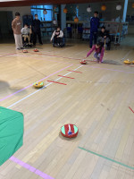 一人の女の子がカーリングのストーンを投げている。周りでは他の参加者が見守っている。