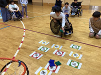 体育館で車いすに乗っている男の子が、点数目掛けて、ビーンバッグ（お手玉）を投げている。
