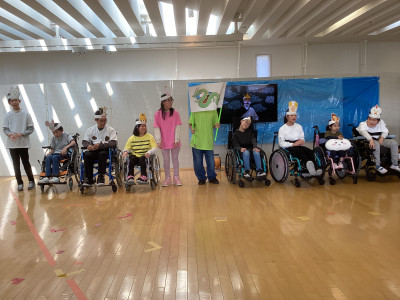 校内で開かれた学部行事公開「オータムフェス２０２５」の発表の様子。十二支の動物のお面を頭にかぶった生徒１０名が、一列に横に並んでいる。生徒の後ろにはモニターがあり、神様のお面をかぶり、ひげを付けた生徒が映っている。