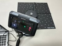 机の上に設置された3DスキャナーREVOPOINTが、小さな岩石をスキャンしている様子。岩石は黒いターンテーブルの上に置かれ、その下には白いドットマーカー付きの黒いマット（Near Mode用）が敷かれている。画面にはリアルタイムでスキャンデータが表示されている。