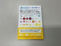 机の上に置かれた『無料データをそのまま3Dプリント　作業に出会える道具カタログ／事例集』という書籍。表紙にはカラフルな3Dプリント作品のシルエットが並び、黄色い帯に『無料！簡単！すぐできる！！』と大きく書かれている。