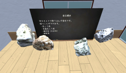メタバース空間に4つの岩石が並び、後ろに黒板が立てられている。黒板には「岩石標本」と書かれ、「3Dスキャナで取り込んだ岩石です。持つことができます。」という説明と、花こう岩、巨晶花こう岩、凝灰岩（大谷石）、蛇紋岩の名前が記されている。室内はシンプルな壁と窓のある空間で、展示のように配置されている。
