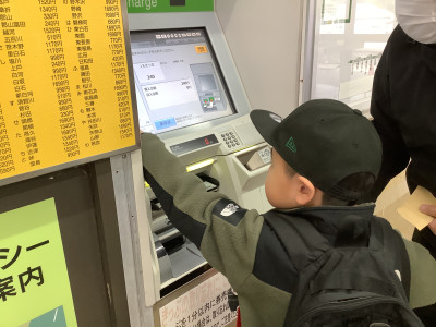 自動券売機にお金を入れてボタンを押して切符を買っています。